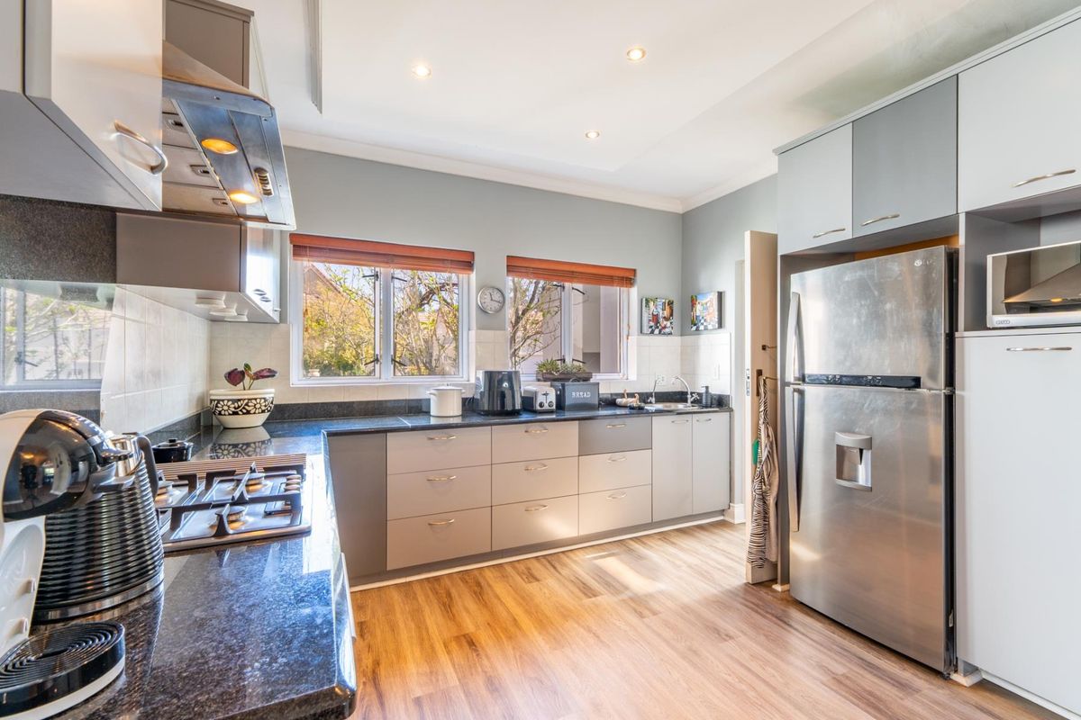 Modern kitchen featuring sleek grey cabinetry, granite countertops, gas hob, extractor fan, and durable laminate flooring with ample natural light.