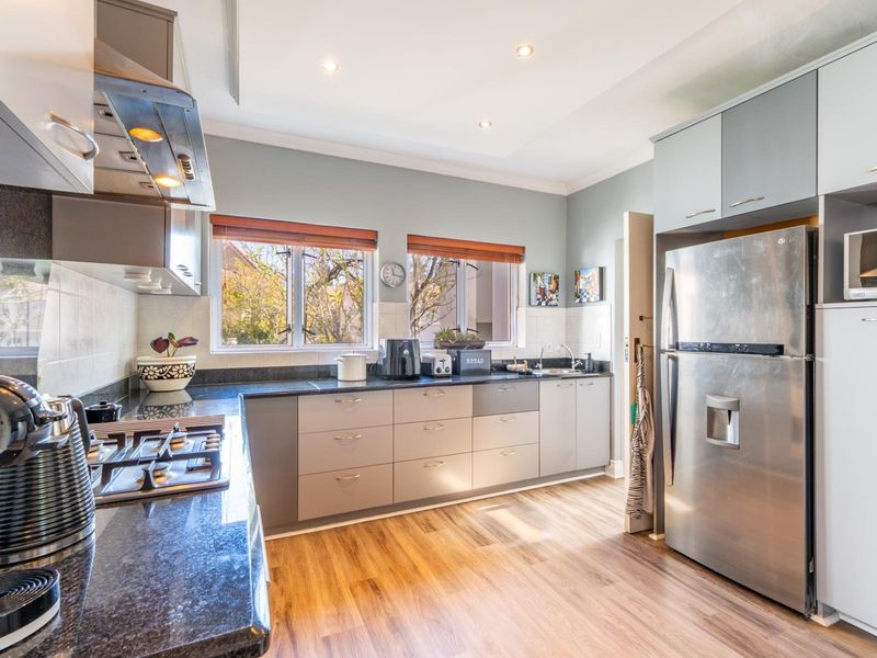 Modern kitchen featuring sleek grey cabinetry, granite countertops, gas hob, extractor fan, and durable laminate flooring with ample natural light.