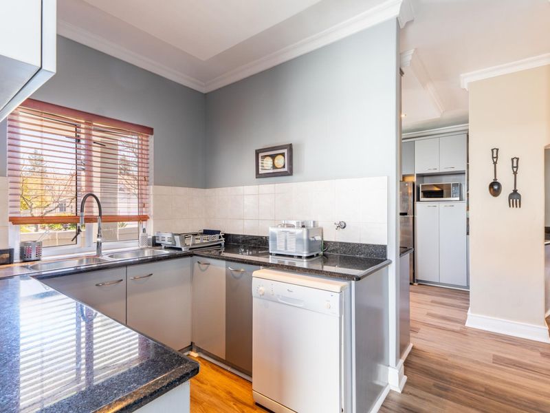 A functional kitchen featuring granite countertops, ample cabinetry, a stainless steel sink, and a tiled backsplash, with an adjacent pantry or scullery area.