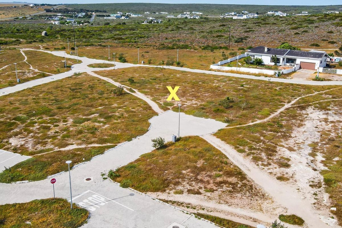 Aerial view of a vacant residential plot featuring established paved access roads, street lighting, and surrounding coastal landscape.