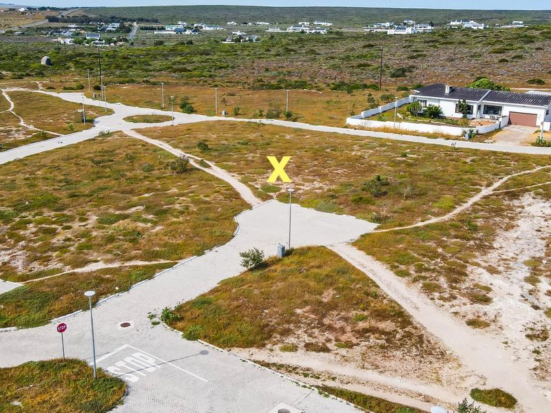Aerial view of a vacant residential plot featuring established paved access roads, street lighting, and surrounding coastal landscape.