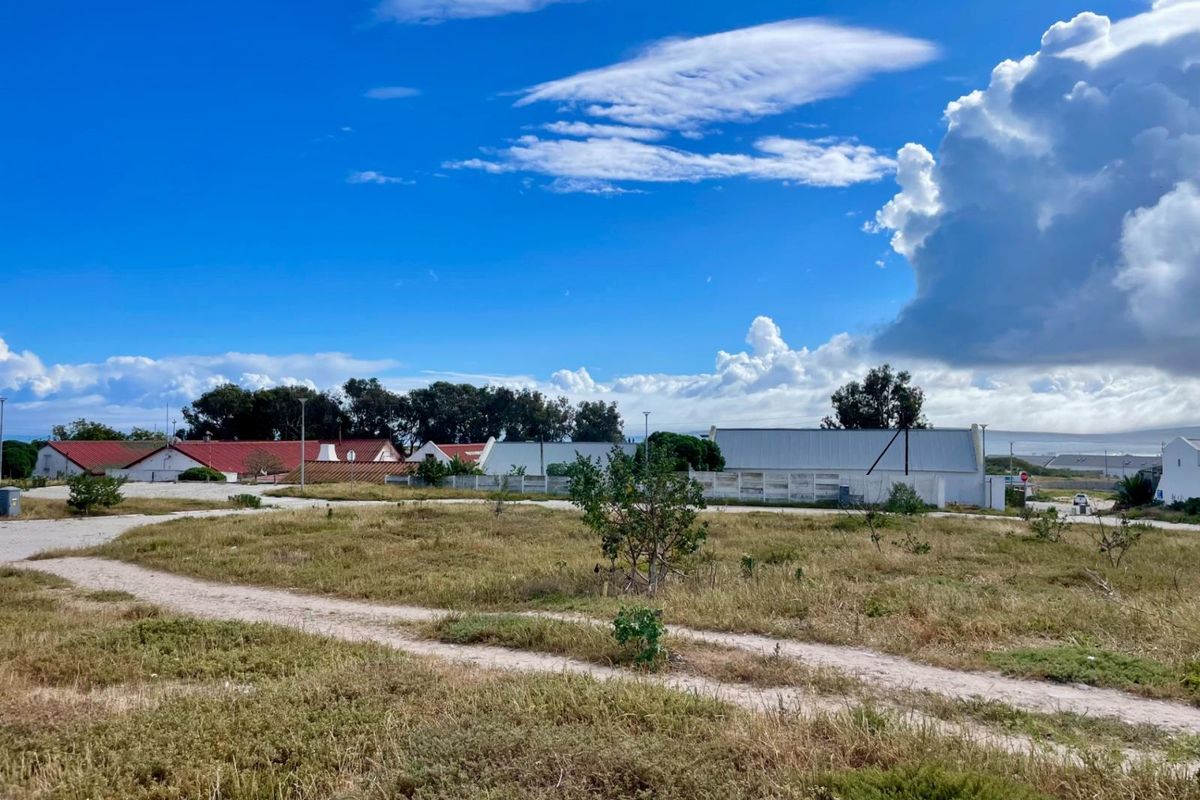 A view of a vacant residential plot featuring natural vegetation and an unpaved access path, situated in a developed neighborhood.