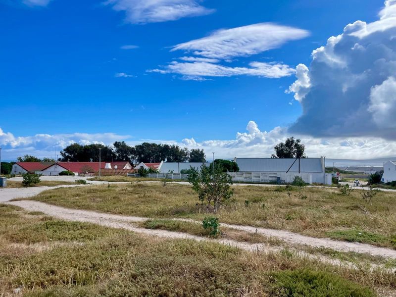 A view of a vacant residential plot featuring natural vegetation and an unpaved access path, situated in a developed neighborhood.
