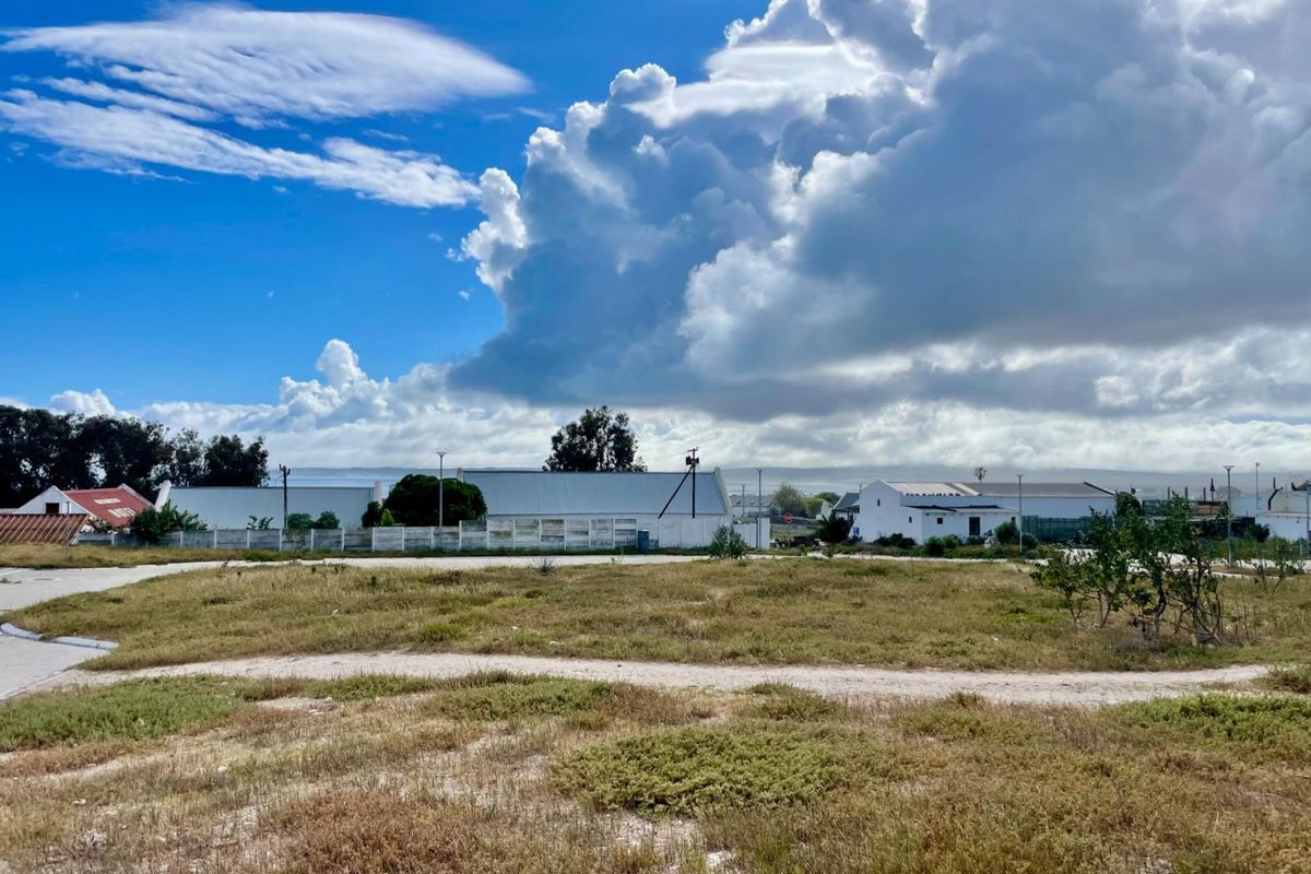 A view of a vacant residential plot of land with surrounding perimeter fencing and nearby neighborhood structures under a cloudy sky.