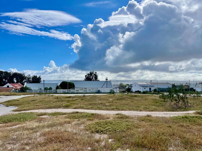 A view of a vacant residential plot of land with surrounding perimeter fencing and nearby neighborhood structures under a cloudy sky.