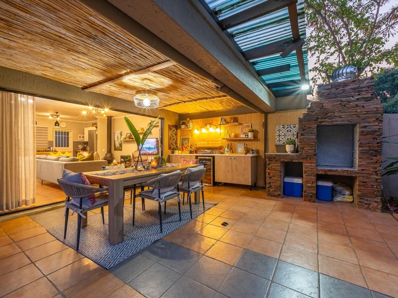 Covered outdoor patio featuring a built-in stone braai, tiled flooring, and a thatched ceiling, seamlessly connecting to the indoor living area via sliding doors.
