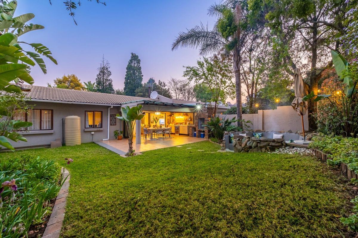 Rear view of the townhouse featuring a landscaped garden, covered patio with built-in braai, and a stone-clad fire pit area.