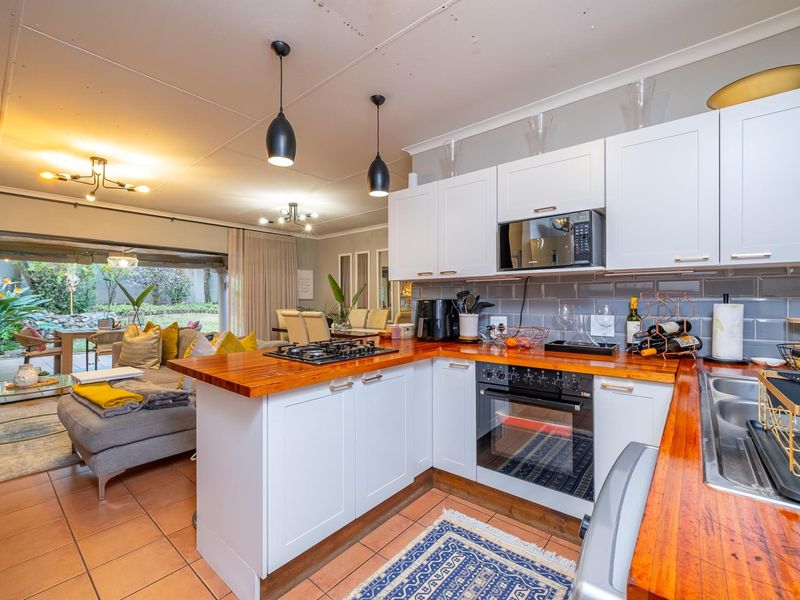 Open-plan kitchen featuring timber countertops, subway tile backsplash, and built-in appliances, flowing seamlessly into a living area with access to a patio.