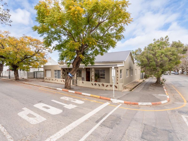 A corner-lot residential property featuring a plastered facade, corrugated metal roof, and a low boundary wall with stone detailing.