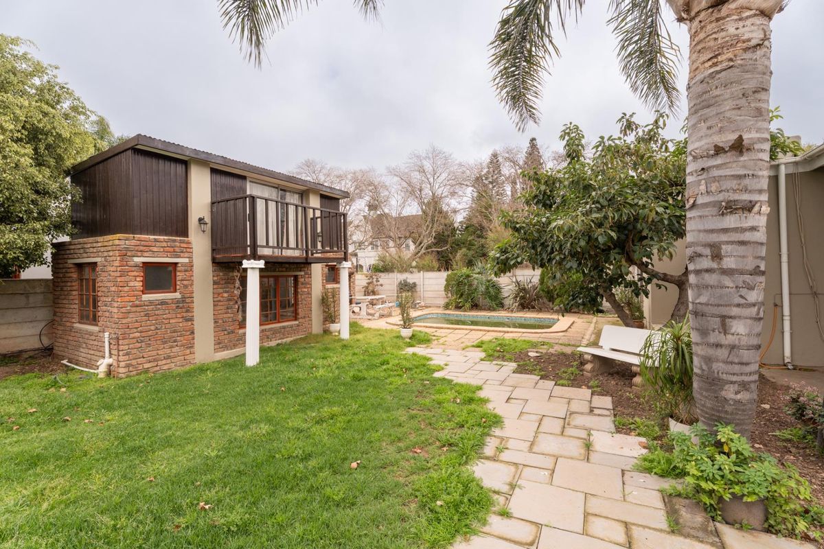 Rear garden view featuring a swimming pool, paved walkway, and a two-story brick structure with an upper-level balcony.