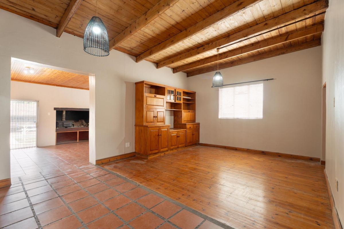 Spacious living area featuring exposed timber beam ceilings, a combination of timber and terracotta flooring, and a built-in fireplace in the adjacent room.
