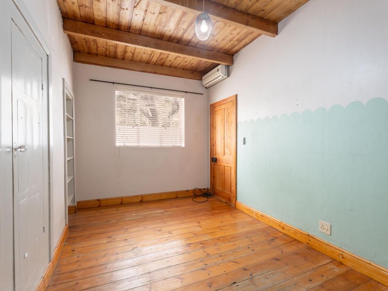 An empty bedroom featuring exposed timber ceiling beams, polished timber flooring, and a wall-mounted air conditioning unit.