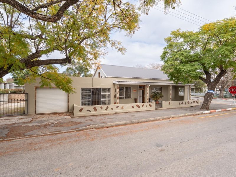 Front exterior view of a single-story house featuring a metal roof, attached garage, and a covered porch area with a low perimeter wall.