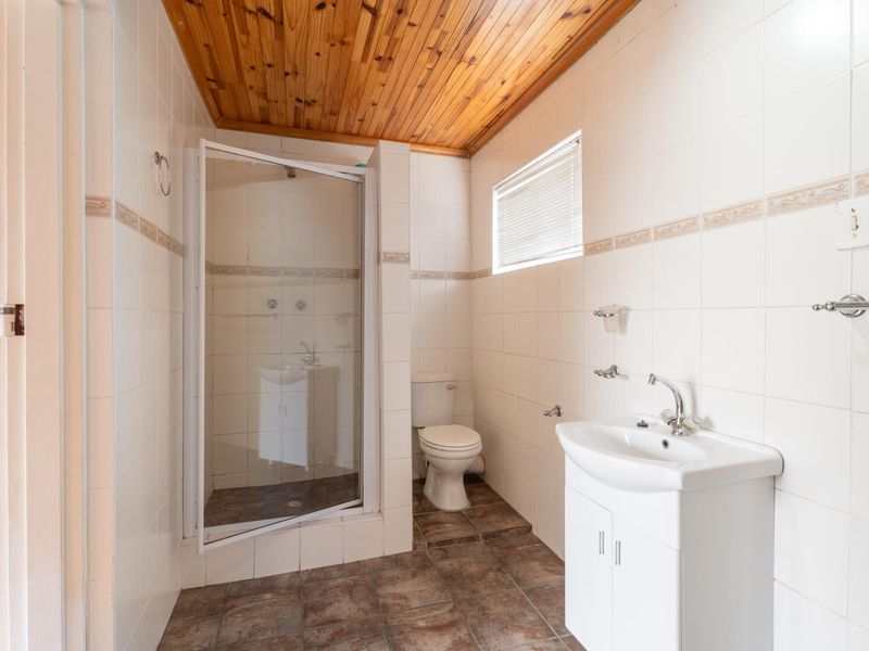A functional bathroom featuring a shower enclosure, toilet, and vanity basin with tiled finishes and a timber ceiling.