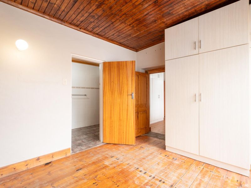 A bedroom featuring timber flooring, a wood-paneled ceiling, and built-in cupboards, with direct access to an adjoining bathroom.