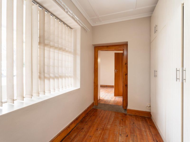 A bright hallway featuring polished hardwood flooring, built-in storage cupboards, and a view through to an adjoining room.