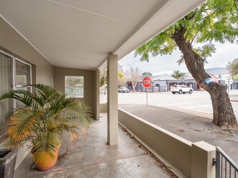 A covered front patio area featuring a concrete floor and low perimeter wall, offering a view of the street and neighborhood.