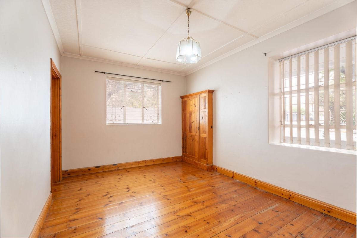 A bright, empty bedroom featuring original timber flooring, built-in cabinetry, and security bars on the windows.