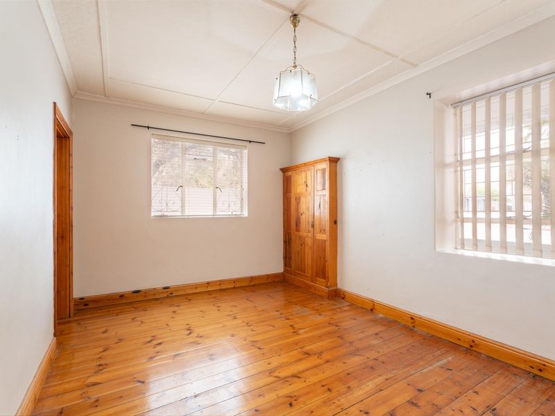 A bright, empty bedroom featuring original timber flooring, built-in cabinetry, and security bars on the windows.