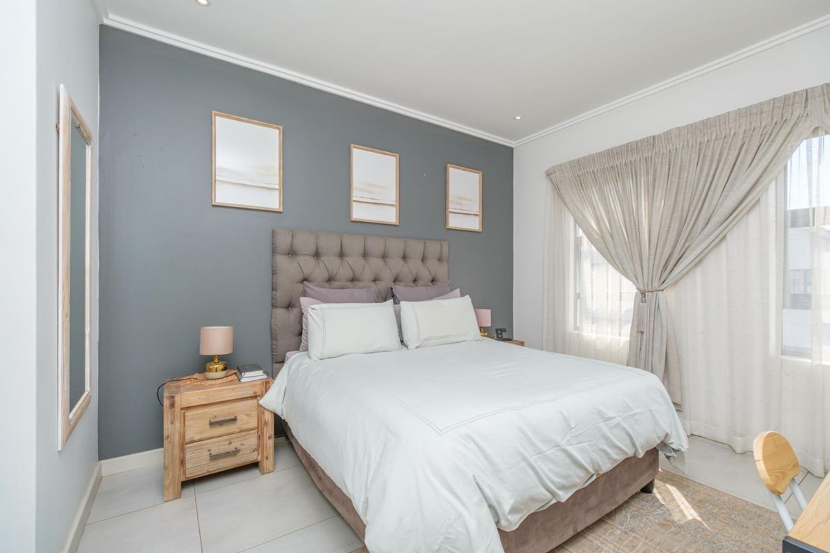 A well-maintained bedroom featuring neutral tiled flooring, a grey feature wall, and recessed downlighting, creating a comfortable and modern living space.