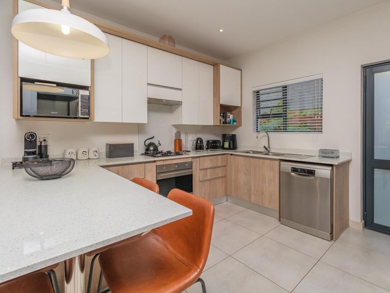 Modern kitchen featuring sleek white and wood-tone cabinetry, stone countertops, integrated appliances, and a breakfast bar, finished with contemporary tiled flooring.