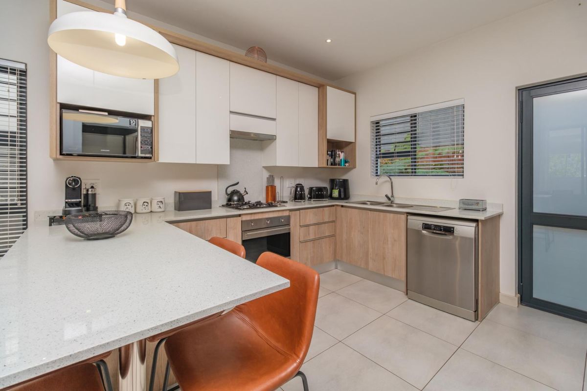 Modern kitchen featuring sleek white and wood-tone cabinetry, stone countertops, integrated appliances, and a breakfast bar, finished with contemporary tiled flooring.