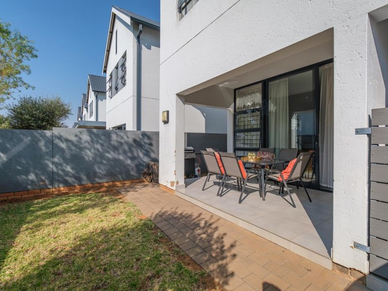 A covered patio area with tiled flooring, leading out to a small private garden with a paved walkway and boundary wall.