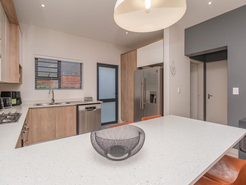 Modern kitchen featuring quartz countertops, light wood cabinetry, integrated appliances, and a central island, offering a clean and functional culinary space.