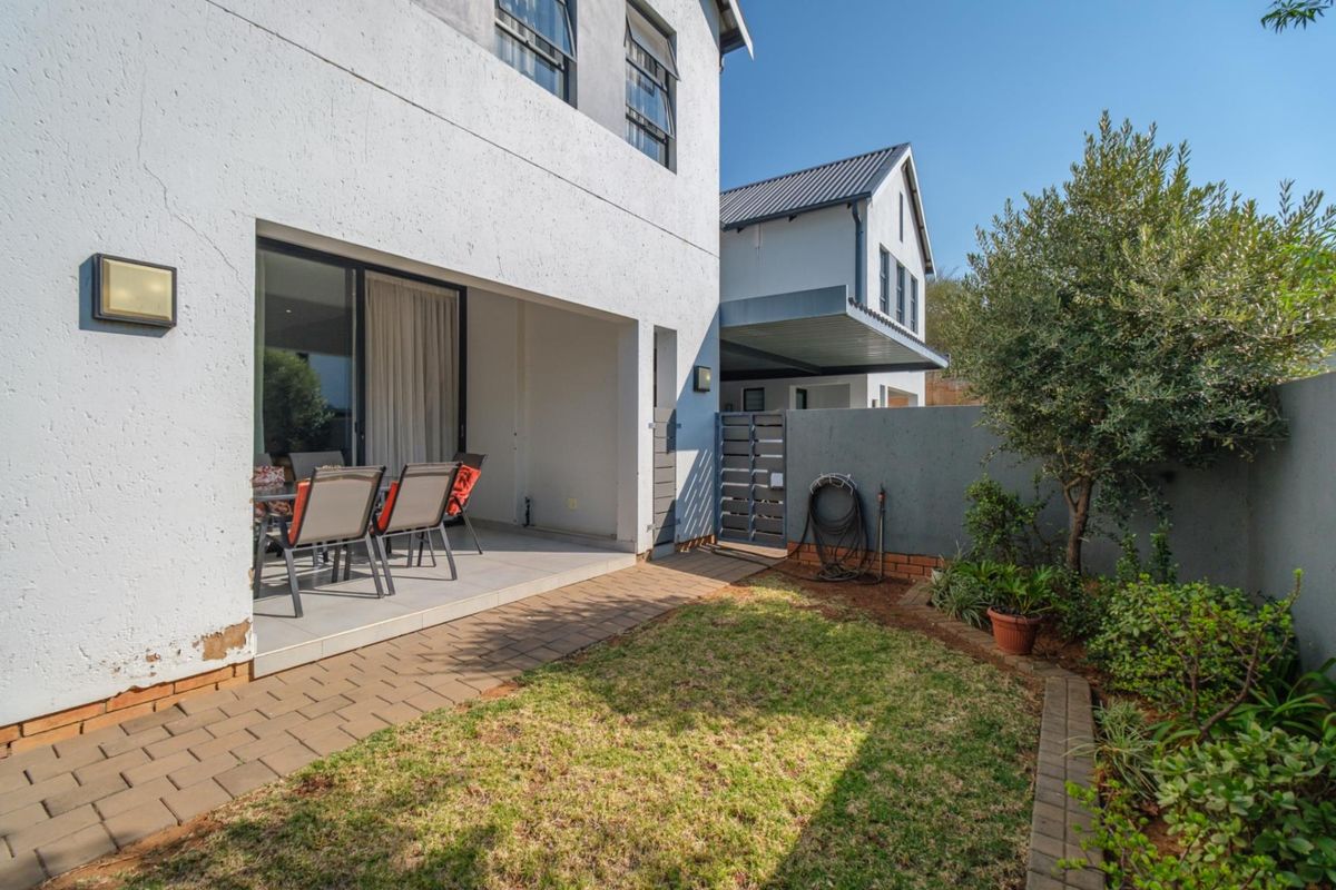 Rear view of the townhouse featuring a covered patio, paved walkway, small garden area, and secure boundary wall with a metal gate.