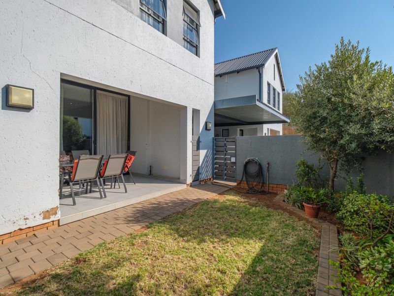 Rear view of the townhouse featuring a covered patio, paved walkway, small garden area, and secure boundary wall with a metal gate.