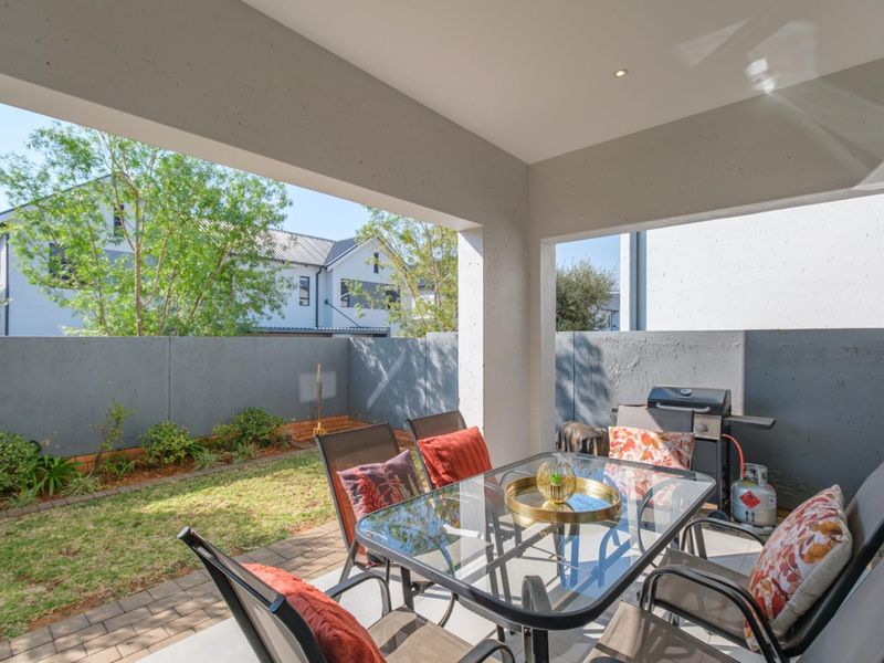 A covered patio area featuring paved flooring and recessed lighting, overlooking a private garden with a boundary wall.