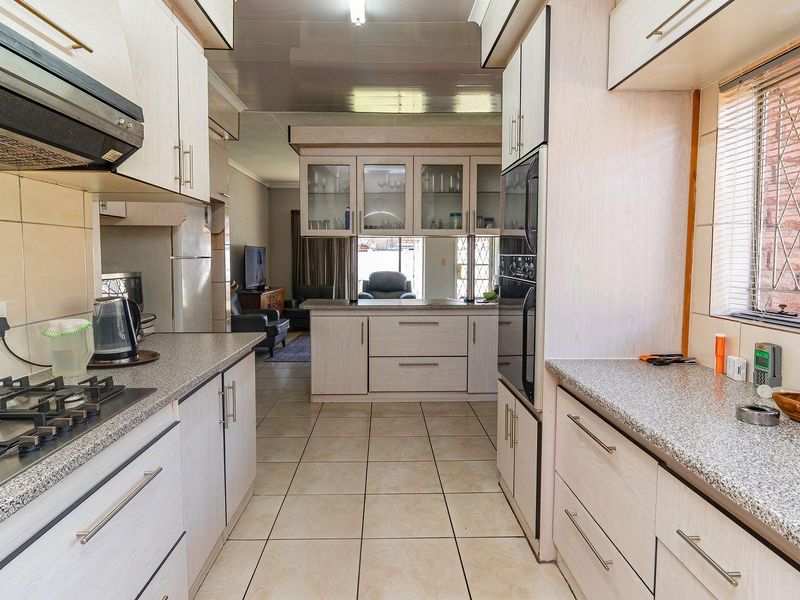 Functional kitchen featuring light-toned cabinetry, granite countertops, a gas hob, and built-in oven, with an open-plan layout connecting to the living area.