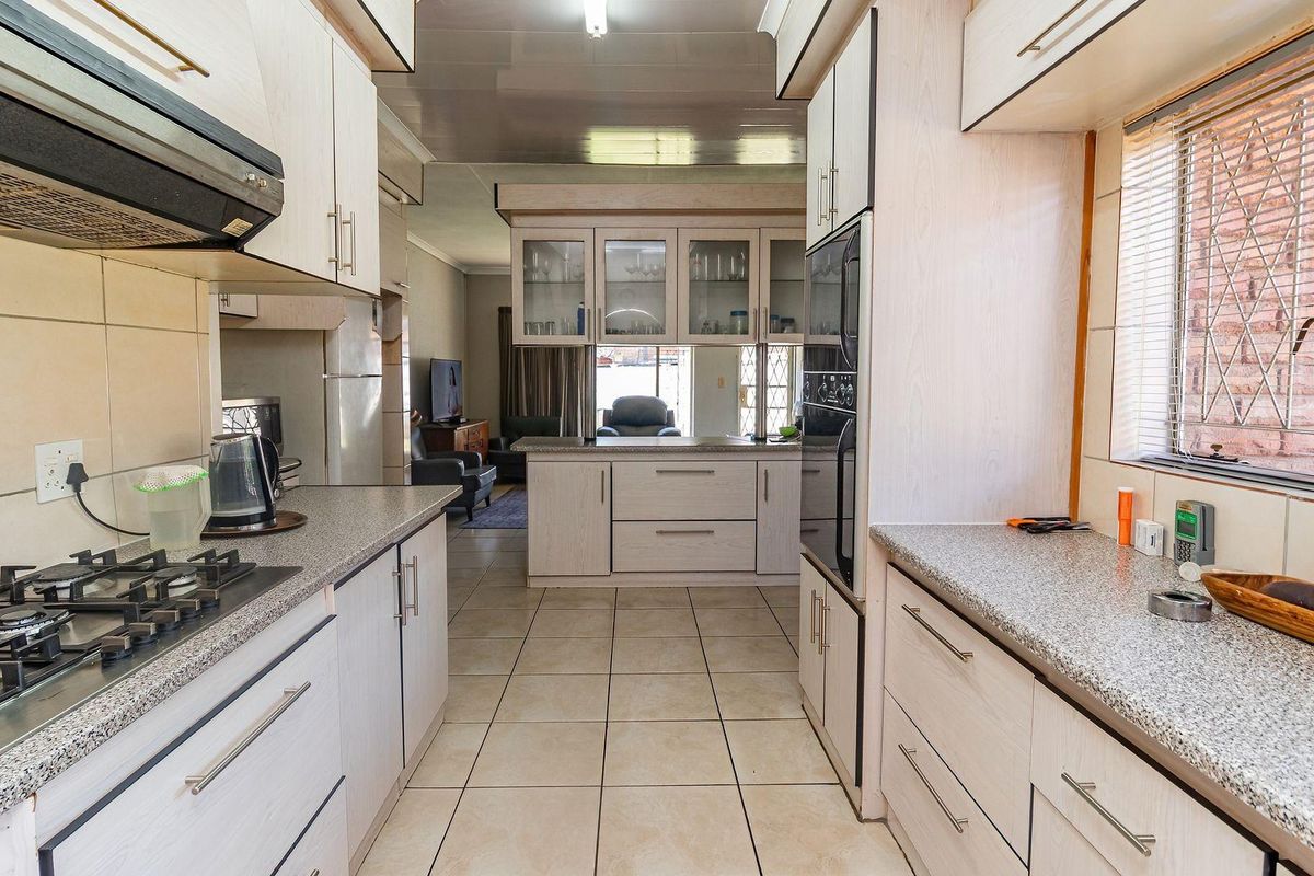 Functional kitchen featuring light-toned cabinetry, granite countertops, a gas hob, and built-in oven, with an open-plan layout connecting to the living area.