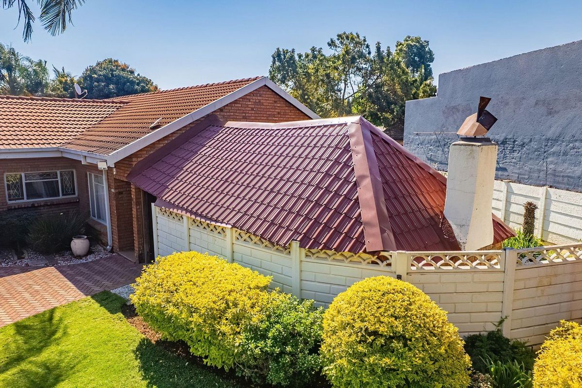 Rear view of the property featuring a brick facade, tiled roof, chimney stack, and a paved courtyard area with established garden landscaping.