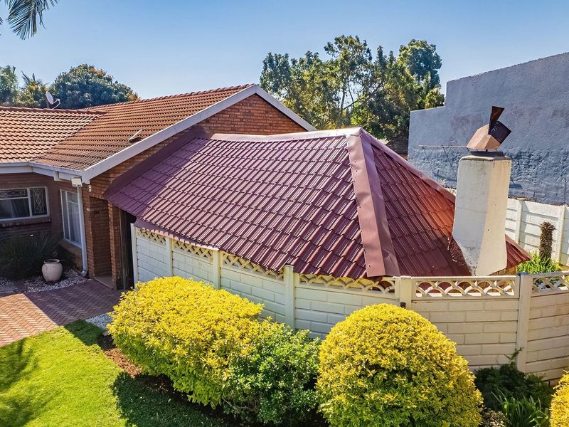 Rear view of the property featuring a brick facade, tiled roof, chimney stack, and a paved courtyard area with established garden landscaping.