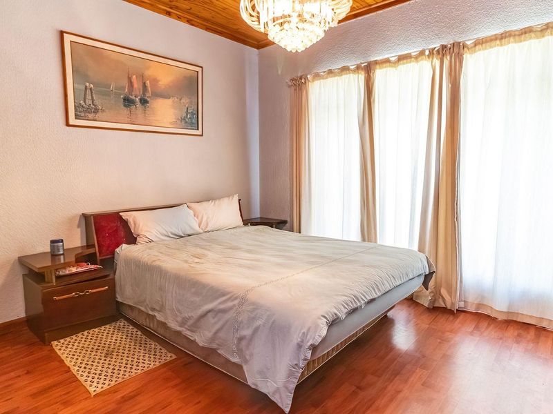 A bedroom featuring warm laminate flooring, a timber-paneled ceiling, and a decorative crystal chandelier, offering a cozy and traditional atmosphere.