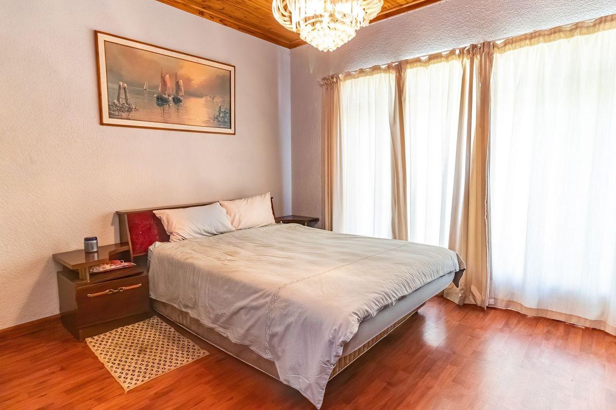 A bedroom featuring warm laminate flooring, a timber-paneled ceiling, and a decorative crystal chandelier, offering a cozy and traditional atmosphere.