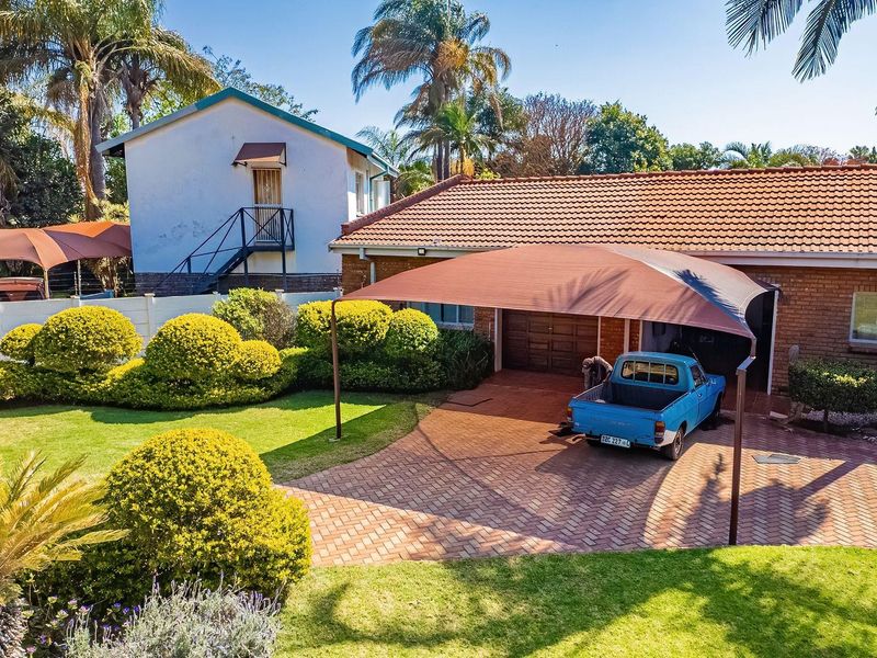 Front view of the property featuring a brick driveway, shade sail carport, and established garden with a tiled roof house facade.