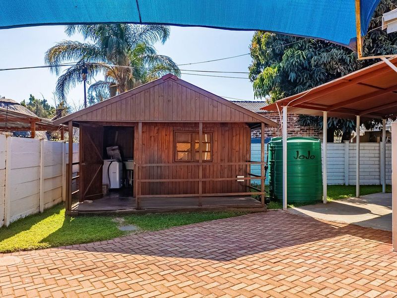 Rear garden area featuring a wooden cabin, paved driveway, water storage tank, and a covered patio area with shade sail.