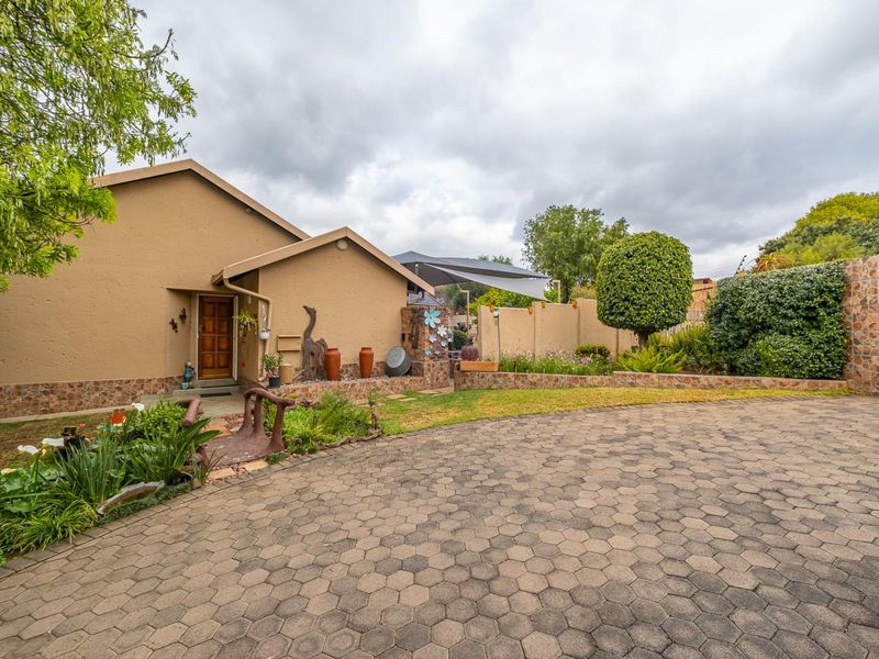 Front exterior view of the house featuring a paved driveway, stone-clad accents, and a well-maintained garden with a timber entrance door.