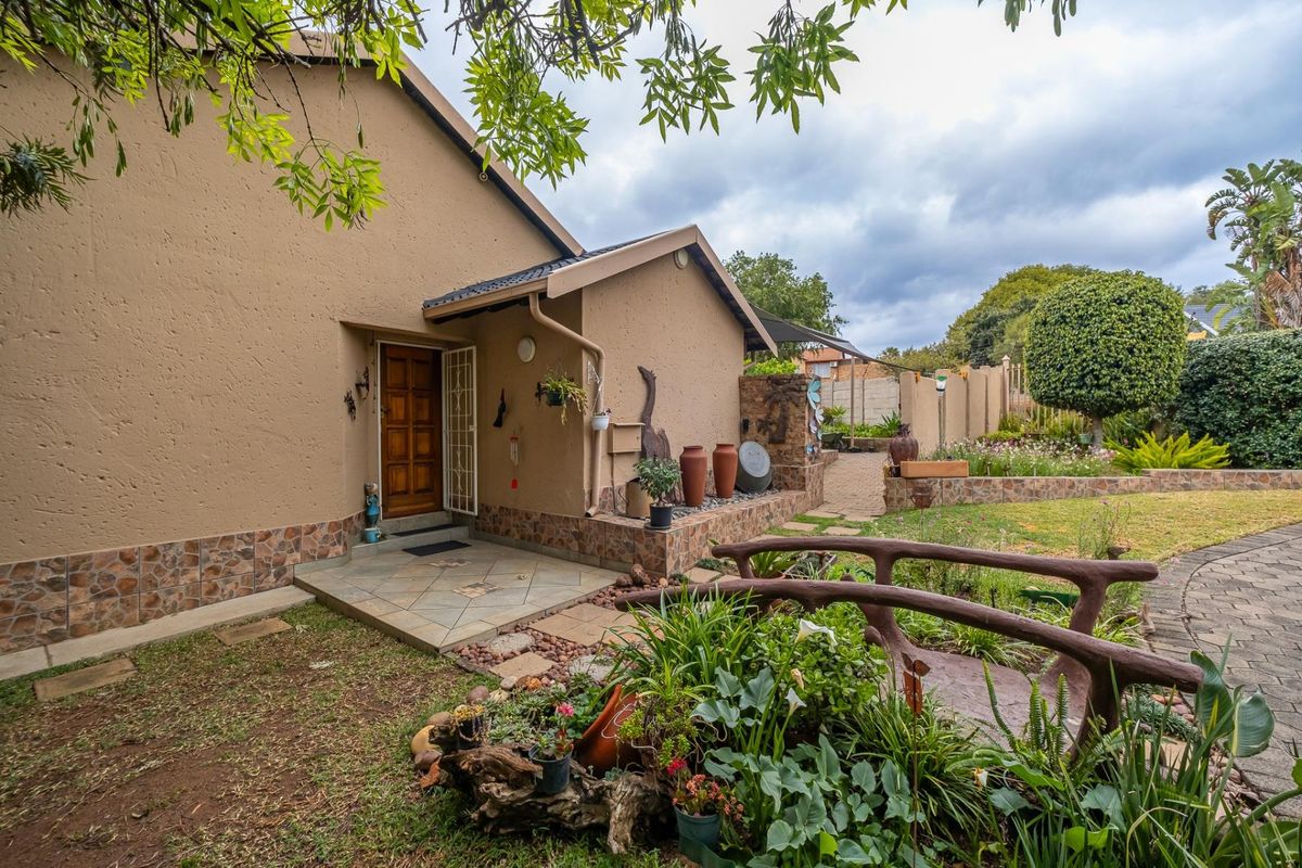 A well-maintained rear exterior view featuring a tiled entrance porch, stone-clad base, and a beautifully landscaped garden with a decorative bridge and paved pathways.