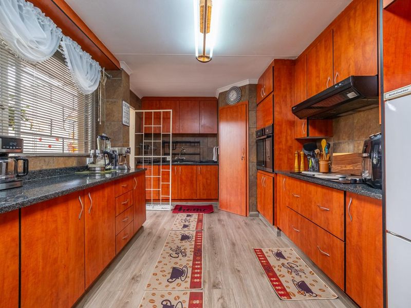 A functional kitchen featuring warm-toned laminate cabinetry, granite countertops, built-in oven, extractor fan, and durable laminate flooring.