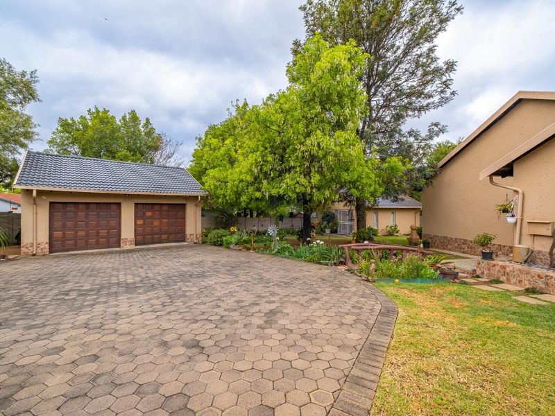 Front view of the property featuring a spacious paved driveway, a double garage with wooden doors, and a well-maintained garden area.