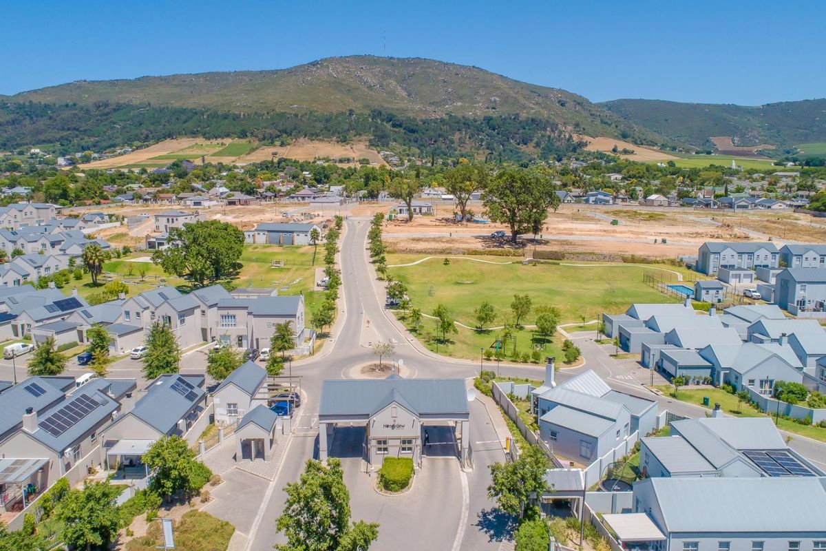 Aerial view of a modern residential estate featuring a secure gated entrance, paved streets, and surrounding mountain landscape.
