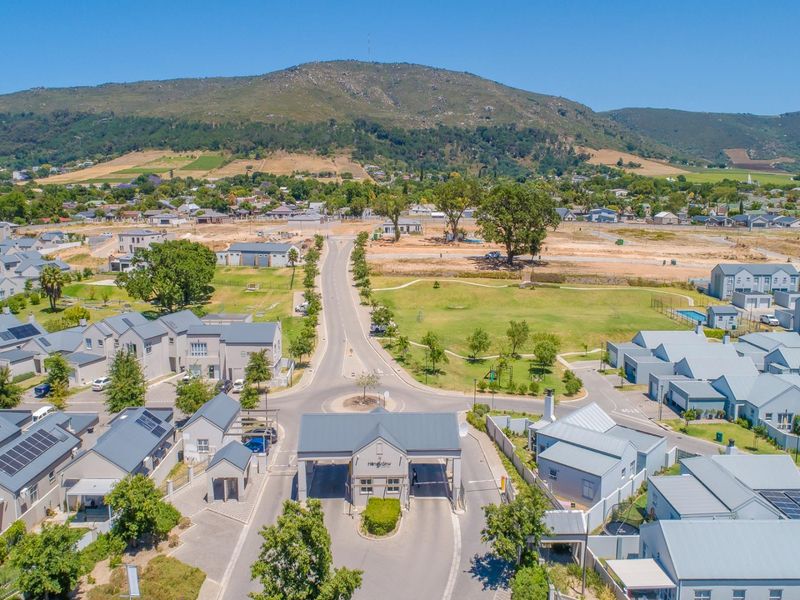 Aerial view of a modern residential estate featuring a secure gated entrance, paved streets, and surrounding mountain landscape.