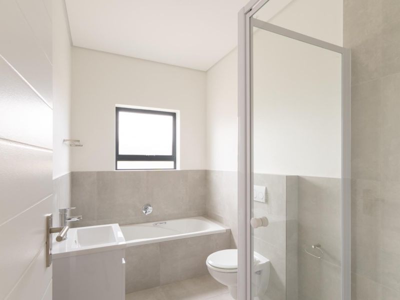 Modern bathroom featuring a built-in bathtub, wall-hung toilet, vanity basin, and a glass-enclosed shower with neutral tiling.
