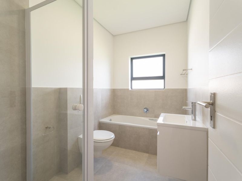 Modern bathroom featuring a built-in bathtub, wall-hung toilet, vanity with basin, and a glass-enclosed shower with neutral floor-to-ceiling tiling.