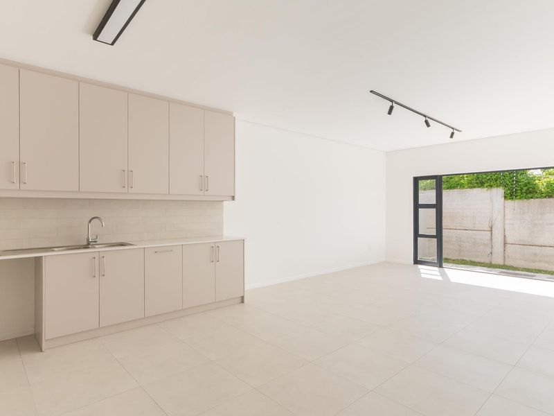 Modern open-plan kitchen and living area featuring neutral cabinetry, tiled flooring, and bi-fold doors opening to an outdoor space.