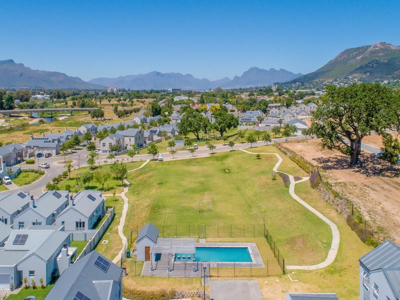 Aerial view of a residential estate featuring a communal swimming pool, landscaped green space, and surrounding modern homes with mountain views.