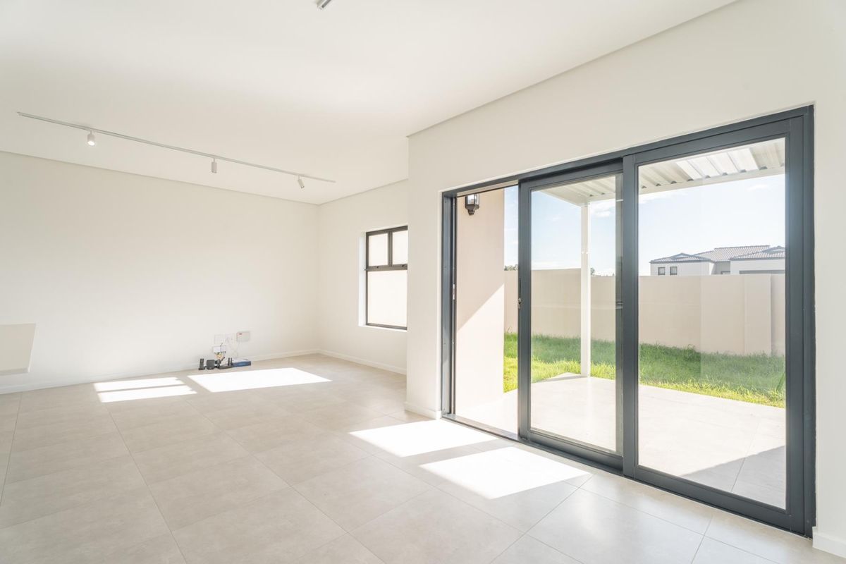 Bright and spacious open-plan living area featuring modern tiled flooring, track lighting, and large sliding glass doors leading to an outdoor patio.